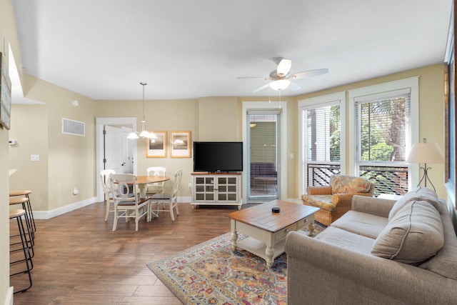 living area featuring ceiling fan with notable chandelier, wood finished floors, visible vents, and baseboards