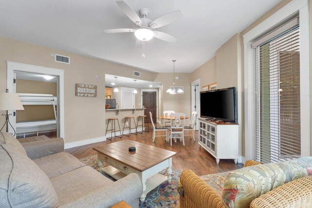 living area with ceiling fan with notable chandelier, wood finished floors, and visible vents