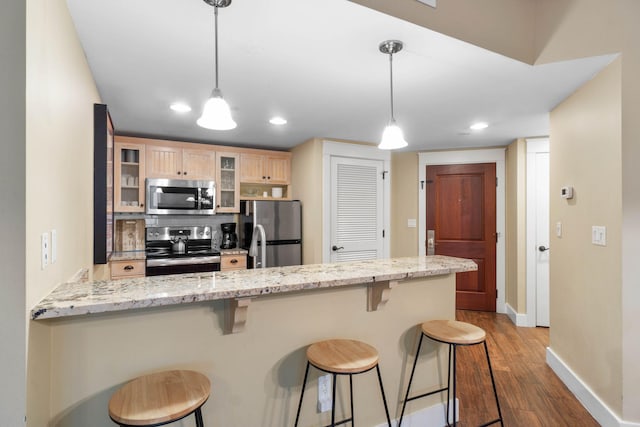 kitchen featuring wood finished floors, a peninsula, stainless steel appliances, glass insert cabinets, and a kitchen breakfast bar