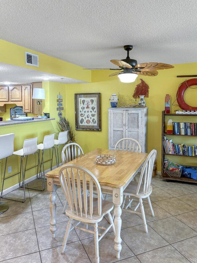 dining area featuring light tile patterned floors, visible vents, ceiling fan, a textured ceiling, and baseboards