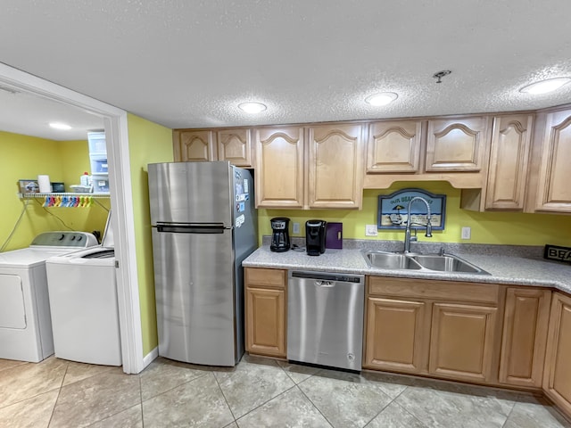 kitchen featuring light tile patterned floors, appliances with stainless steel finishes, a textured ceiling, separate washer and dryer, and a sink