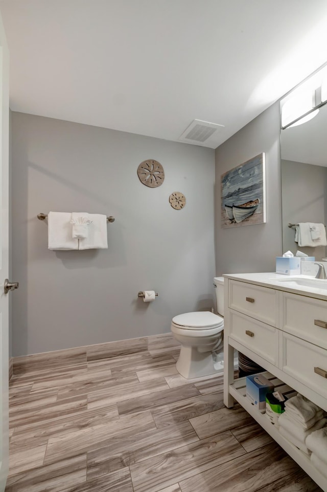 bathroom featuring visible vents, baseboards, toilet, wood finished floors, and vanity