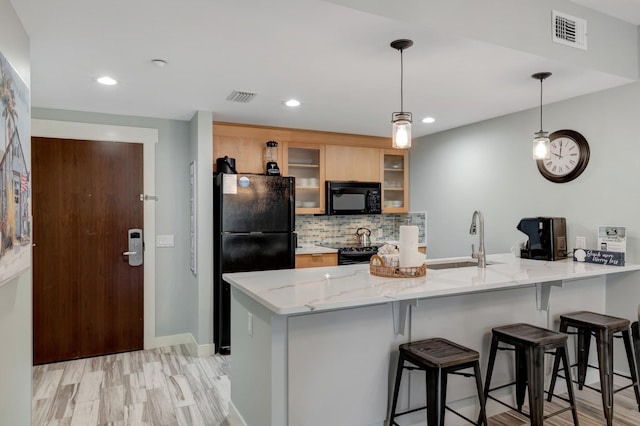 kitchen with black appliances, a peninsula, visible vents, and a sink