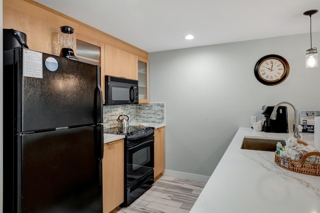 kitchen featuring light brown cabinetry, decorative backsplash, light wood-style flooring, black appliances, and a sink