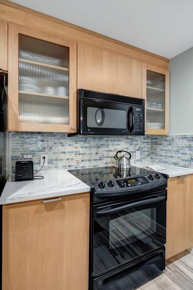 kitchen featuring black appliances, glass insert cabinets, and tasteful backsplash