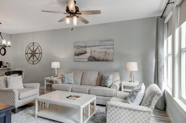 living area with baseboards, wood finished floors, and ceiling fan with notable chandelier