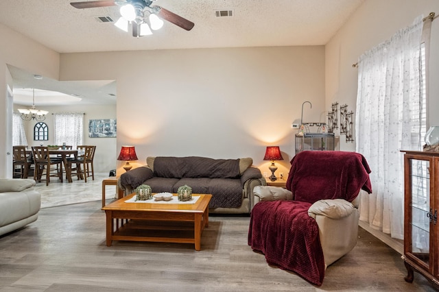 living room featuring ceiling fan with notable chandelier, visible vents, a textured ceiling, and wood finished floors