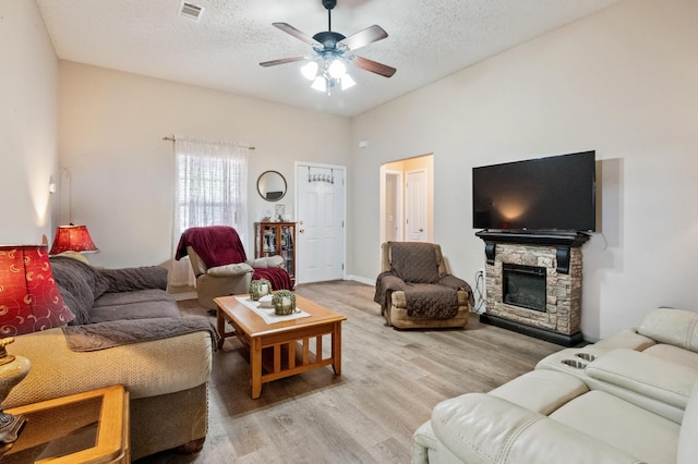 living room with a fireplace, visible vents, light wood-style flooring, ceiling fan, and a textured ceiling