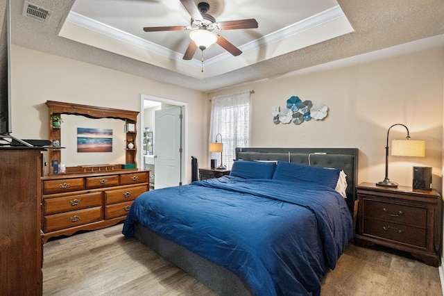 bedroom with a raised ceiling, visible vents, crown molding, and wood finished floors