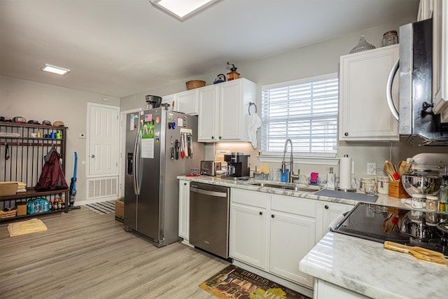 kitchen with light wood finished floors, visible vents, white cabinets, stainless steel appliances, and a sink