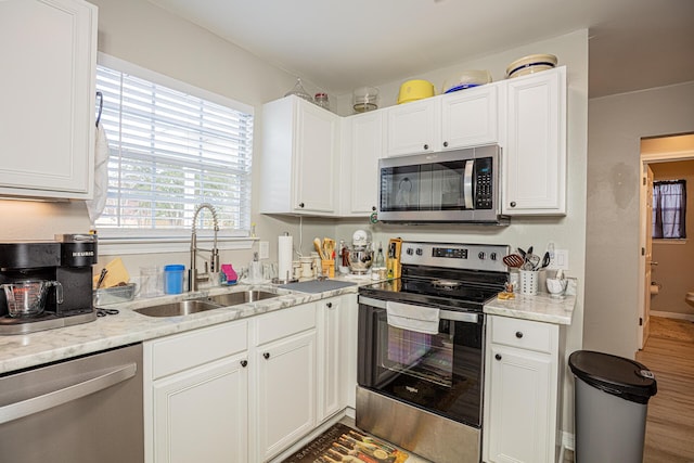 kitchen with a sink, wood finished floors, stainless steel appliances, white cabinets, and light stone countertops