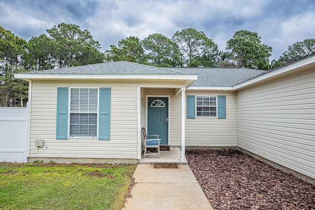 property entrance with a shingled roof, a yard, and fence