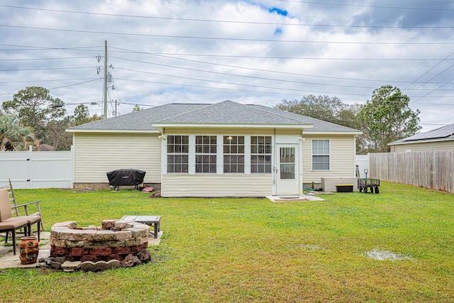 back of property with a fire pit, a yard, a fenced backyard, and a shingled roof