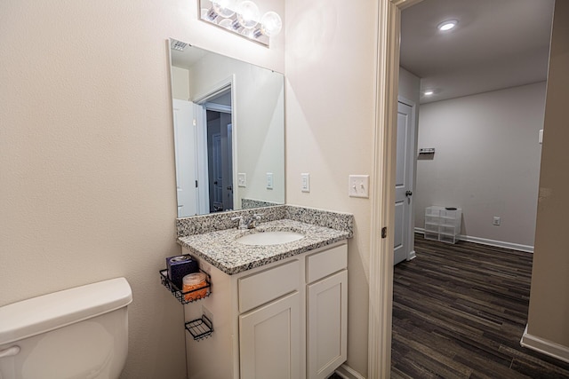 half bathroom featuring toilet, vanity, baseboards, and wood finished floors