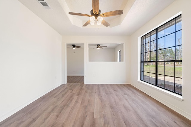 unfurnished room featuring light wood-style floors, baseboards, and a raised ceiling