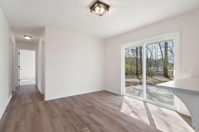 unfurnished dining area featuring a textured ceiling, baseboards, and wood finished floors