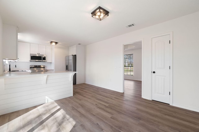 kitchen with stainless steel appliances, light countertops, visible vents, a sink, and wood finished floors