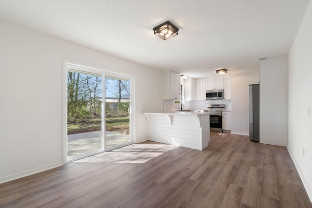 kitchen with white cabinets, a peninsula, stainless steel appliances, light countertops, and a sink