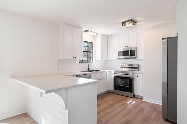 kitchen featuring decorative backsplash, white cabinets, a peninsula, stainless steel appliances, and a sink