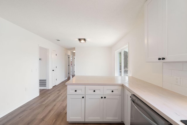 kitchen featuring tasteful backsplash, dishwasher, a peninsula, light countertops, and white cabinetry