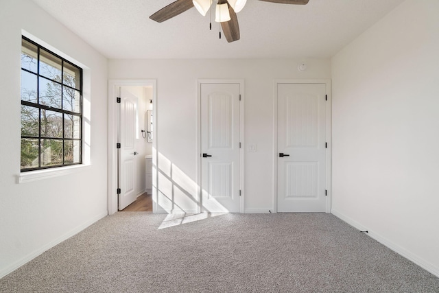 unfurnished bedroom with carpet floors, ceiling fan, ensuite bath, and baseboards