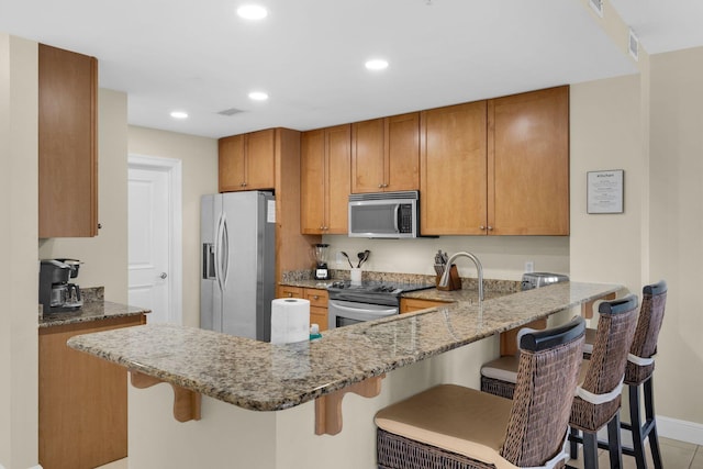 kitchen with appliances with stainless steel finishes, brown cabinets, a peninsula, and light stone countertops