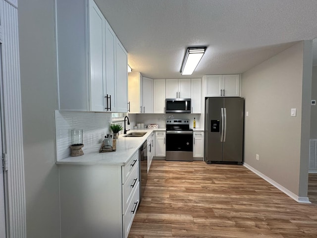 kitchen featuring a sink, stainless steel appliances, white cabinets, light wood-style floors, and tasteful backsplash