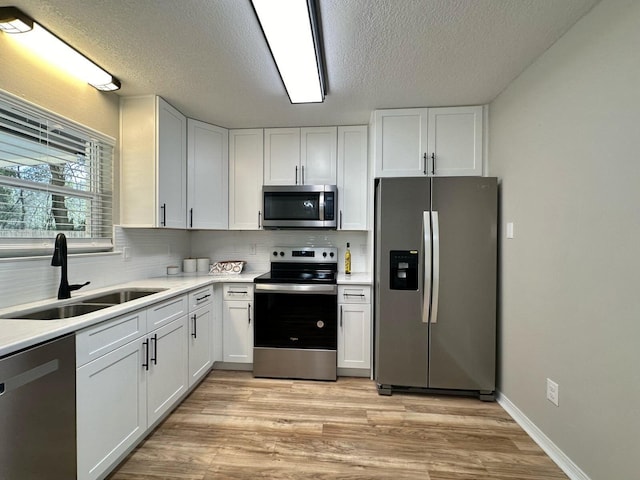 kitchen featuring a sink, stainless steel appliances, light wood finished floors, and white cabinetry