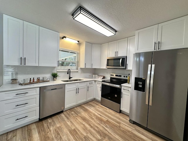 kitchen featuring light wood finished floors, a sink, stainless steel appliances, light countertops, and white cabinets