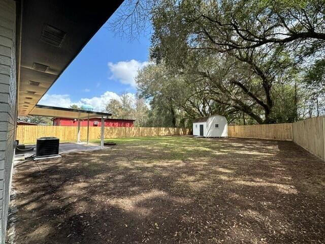 view of yard with central air condition unit, an outdoor structure, a fenced backyard, and a storage shed