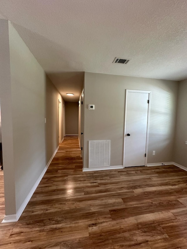 hallway featuring a textured ceiling, wood finished floors, visible vents, and baseboards