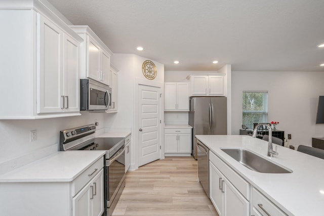 kitchen with appliances with stainless steel finishes, light wood-style floors, white cabinetry, a sink, and recessed lighting