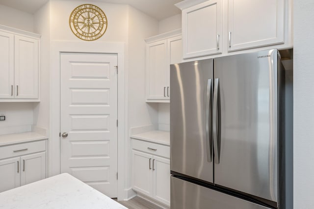 kitchen featuring light stone counters, light wood-type flooring, freestanding refrigerator, and white cabinets