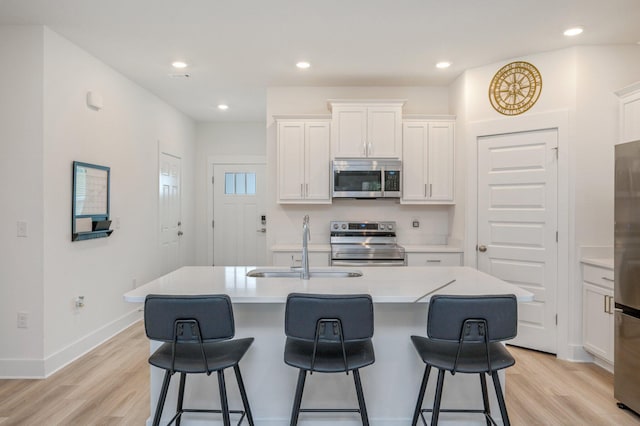 kitchen with a breakfast bar, light wood finished floors, appliances with stainless steel finishes, and white cabinets