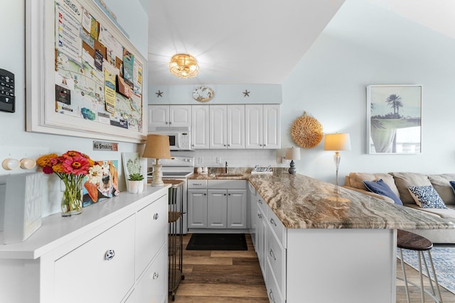 kitchen with a breakfast bar area, electric range, white microwave, white cabinetry, and a peninsula