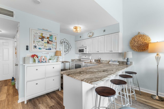 kitchen with white appliances, white cabinets, decorative backsplash, dark wood-type flooring, and a kitchen bar