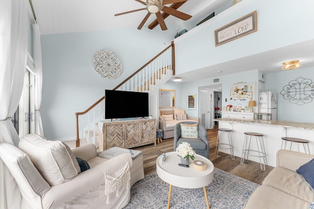 living room with ceiling fan, stairway, a towering ceiling, and wood finished floors