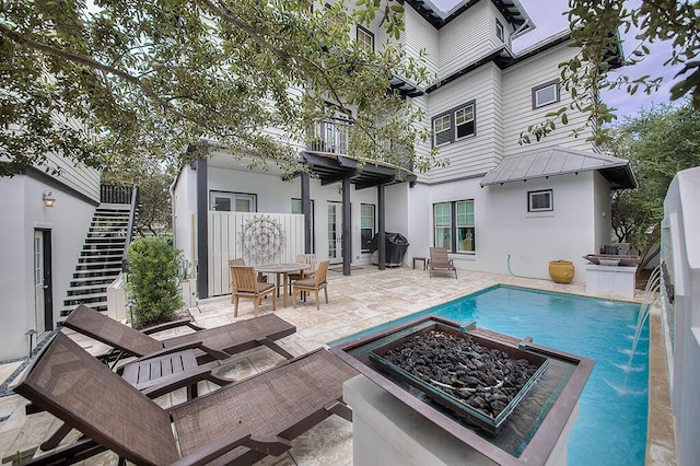 rear view of property featuring stucco siding, a patio, an outdoor fire pit, metal roof, and stairs