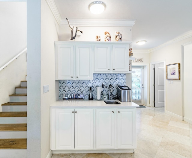 kitchen with a sink, white cabinets, decorative backsplash, and ornamental molding