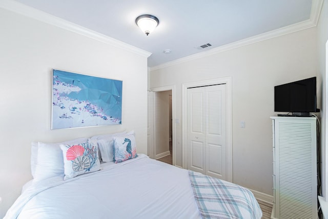 bedroom with visible vents, crown molding, baseboards, wood finished floors, and a closet