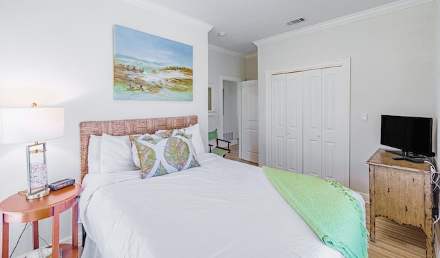 bedroom with a closet, visible vents, wood finished floors, and ornamental molding