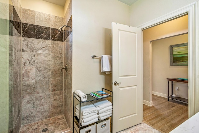 full bathroom with wood finished floors, baseboards, and tiled shower