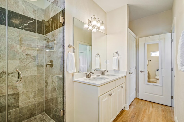 bathroom with a shower stall, wood finished floors, double vanity, and a sink