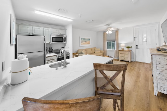 kitchen featuring light stone counters, a breakfast bar, light wood-style flooring, appliances with stainless steel finishes, and a sink