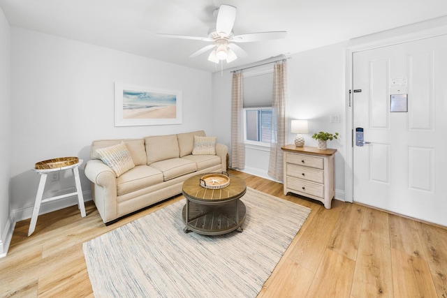 living area featuring a ceiling fan, baseboards, and light wood finished floors