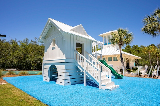 back of property with a playground, fence, and board and batten siding