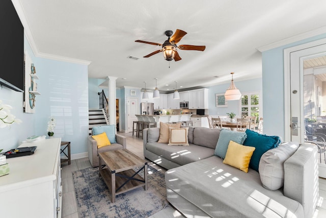 living area featuring visible vents, a ceiling fan, ornamental molding, stairway, and ornate columns