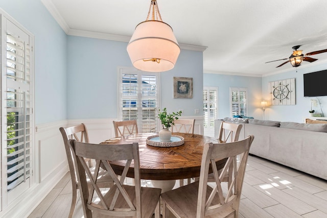 dining space featuring wainscoting, crown molding, a decorative wall, and ceiling fan