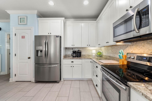 kitchen with tasteful backsplash, appliances with stainless steel finishes, white cabinets, and crown molding