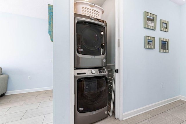 clothes washing area with stacked washer and dryer, wood finish floors, and baseboards